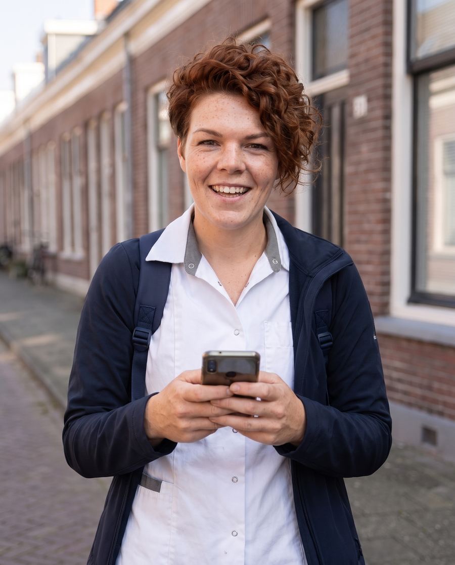 Zorgmedewerker met haar telefoon in de hand, ze lacht in de camera