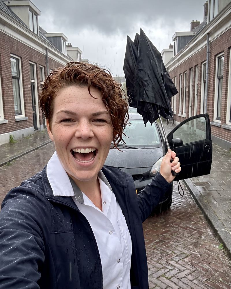 Zorgmedewerker lacht in de regen met een omgewaaide paraplu